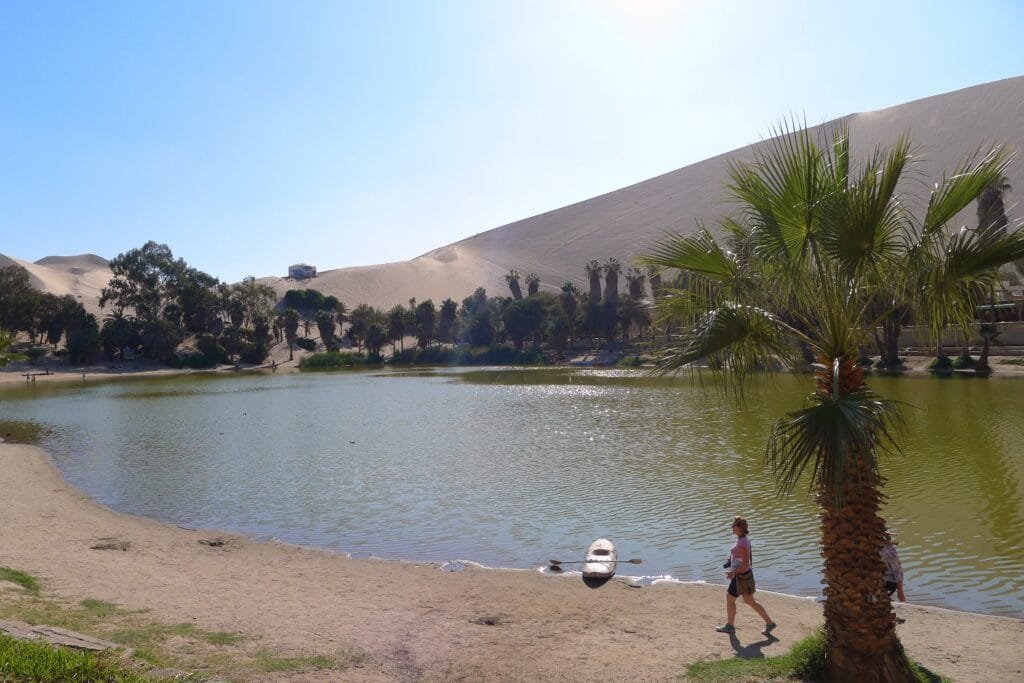 Saving for Travel: How Today’s Sacrifices Create Tomorrow’s Freedom “Traveler at a serene desert oasis in Peru, surrounded by palm trees and clear blue water, symbolizing the rewards of saving for travel.