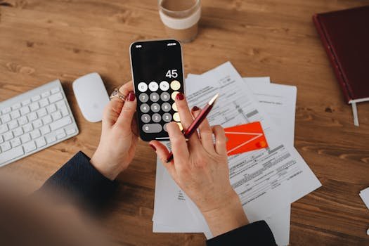 Saving for Travel: How Today’s Sacrifices Create Tomorrow’s Freedom Hands using a calculator app on a smartphone over financial documents. Perfect for illustrating finance or technology themes.
