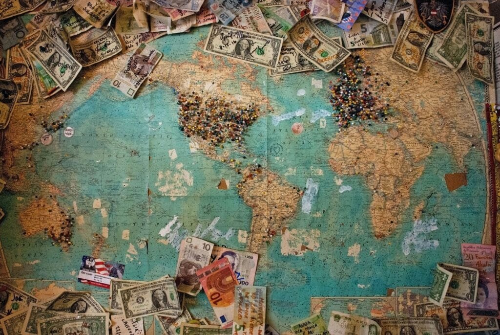 Turning Travel Dreams Into Reality: Choosing a Destination 🧭✈️ World map with various currencies spread across it, illustrating currency value differences for budget travel planning.