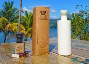 CuloClean portable bidet with reusable bottle displayed outdoors on a tropical wooden table, with palm trees and a lake in the background"